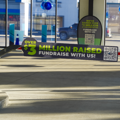 The entrance of Tidal Wave Auto Spa featuring various car wash options on a clear day, with a staff member ready to assist and signage promoting free vacuums with each wash. 